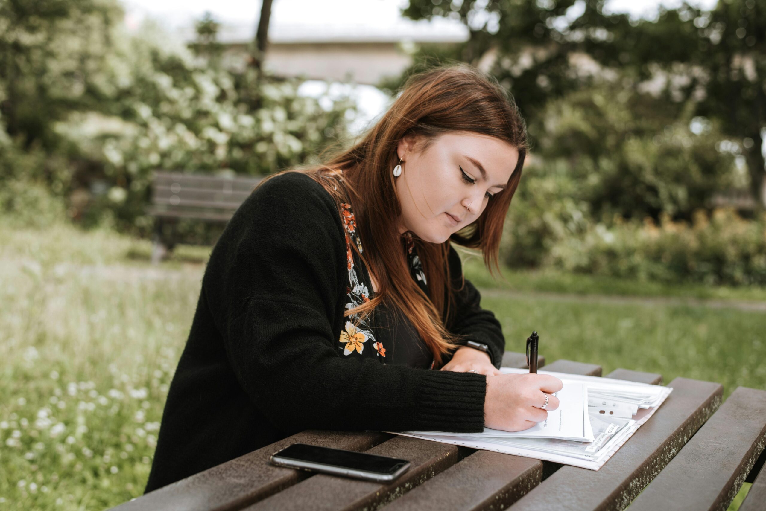Services Focused young woman writing in a notebook while studying outdoors in a summer park.