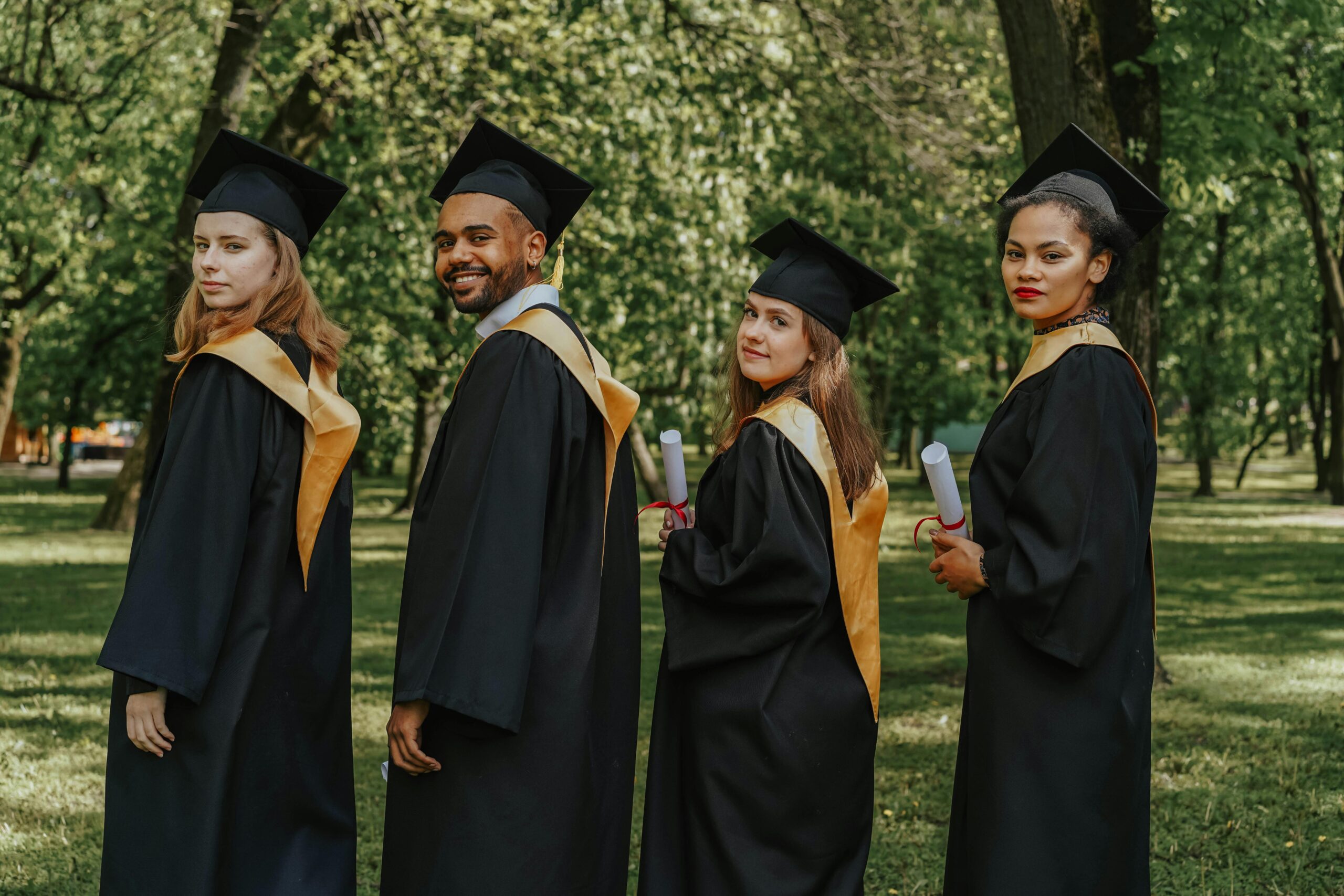 A celebratory group of diverse graduates wearing caps and gowns outdoors, holding diplomas.